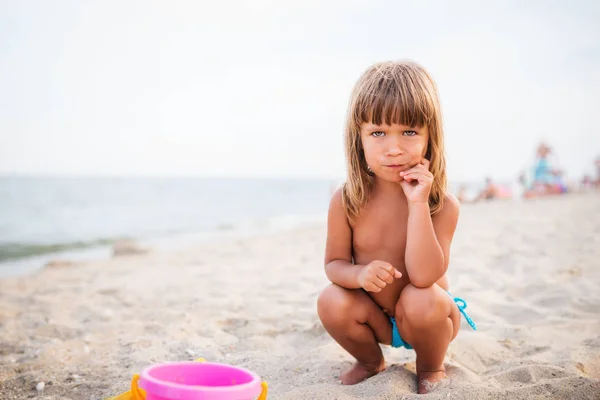 Bambino con espressione divertente siede nella sabbia — Foto Stock