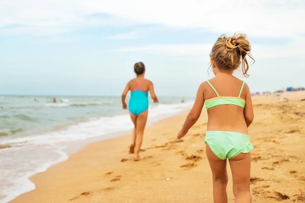 Deux petites filles positives courent le long de la plage de sable — Photo