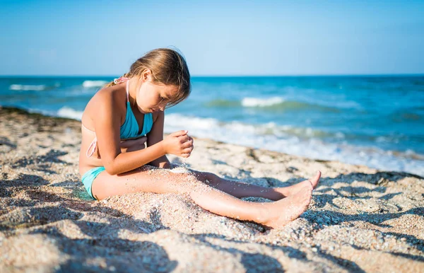 Piccola ragazza positiva siede sulla riva del mare — Foto Stock