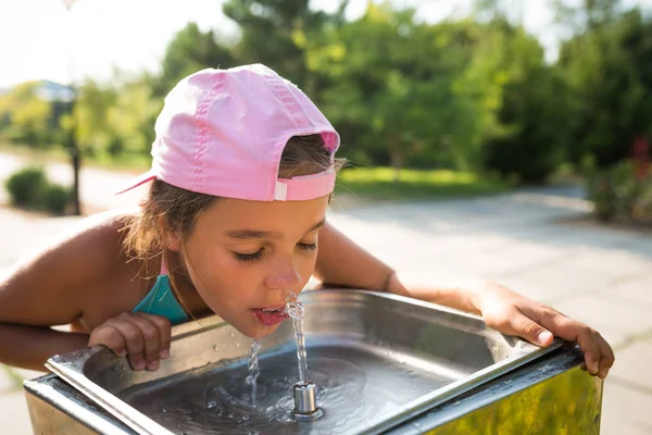 Cute thirsty girl drinks water from drinking sink ロイヤリティフリーのストック写真