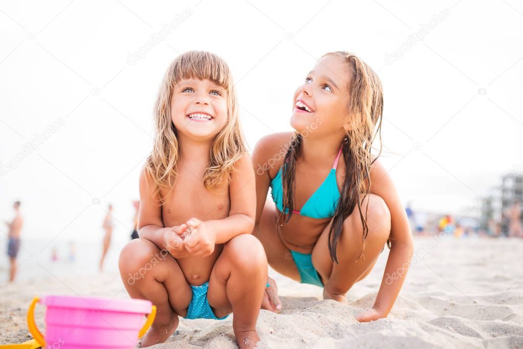 Two girls play on beach while sitting in sand