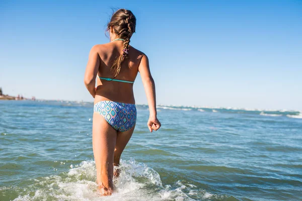 Hátsó nézet a vízen futó pozitív kislányról — Stock Fotó