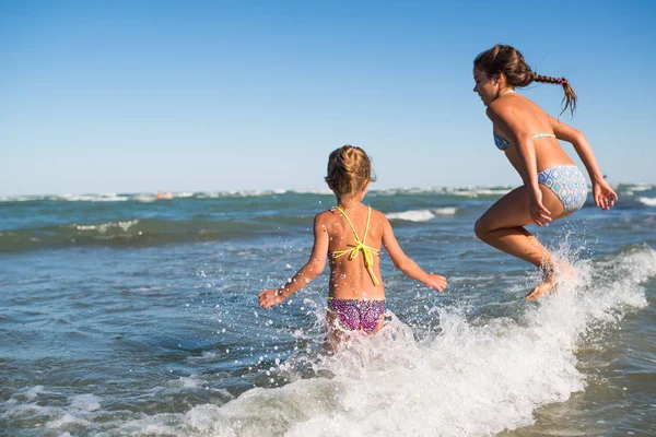 Deux petites filles drôles sautent dans les vagues bruyantes de la mer — Photo