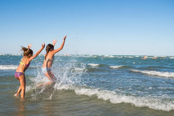 Meninas positivas correm ao longo das ondas tempestuosas — Fotografia de Stock