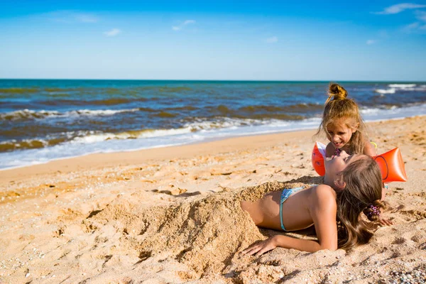 Piccola ragazza allegra seppellire la sorella maggiore nella sabbia — Foto Stock