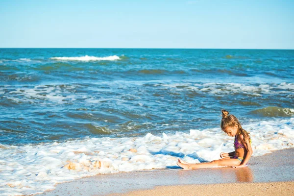Pequeña chica positiva se sienta en la orilla del mar —  Fotos de Stock