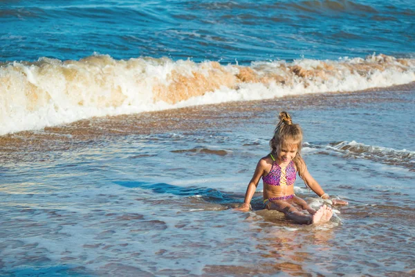 Piccola ragazza positiva siede sulla riva del mare — Foto Stock