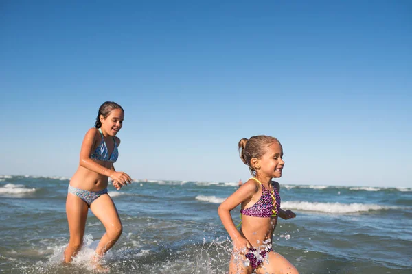 Due divertenti bambine saltano tra le onde rumorose del mare — Foto Stock
