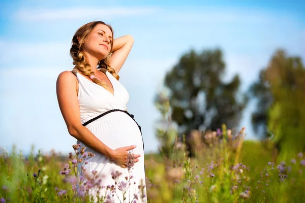 Беременная женщина стоит на цветочном поле — стоковое фото