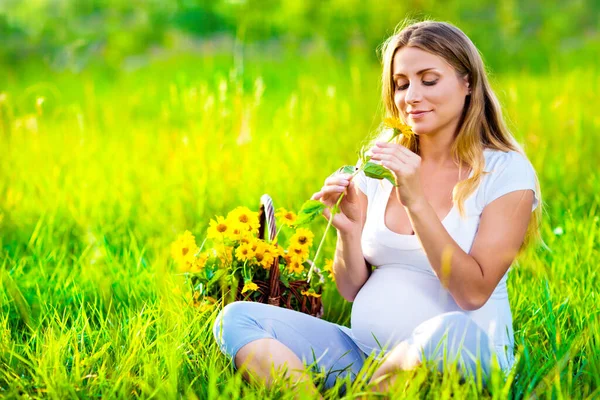 Pregnant woman sitting on green field — Stock Photo, Image