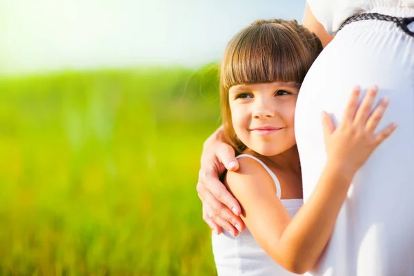 小女孩抱着妈妈怀孕的肚子 — 图库照片