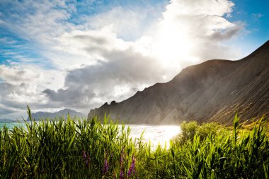 Grass, sea and mountains at background. Cloudy sky