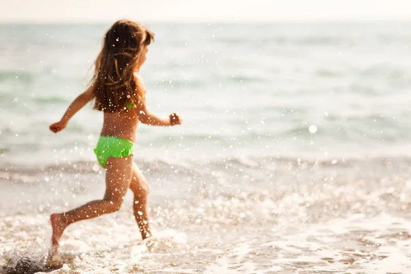 Chica con el pelo castaño correr a lo largo de la orilla del mar — Foto de Stock