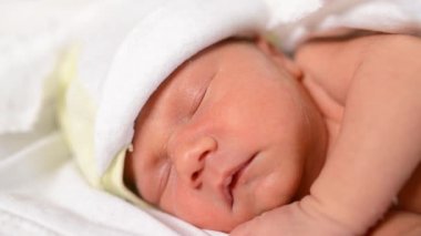 Beyaz dantelli çarşaflarda kestirip duran yeni doğmuş şirin bebeğe yakın çekim. Beyaz bir bezin içinde dinlenen tatlı bir çocuk. Uyuyan bebek kavramı.