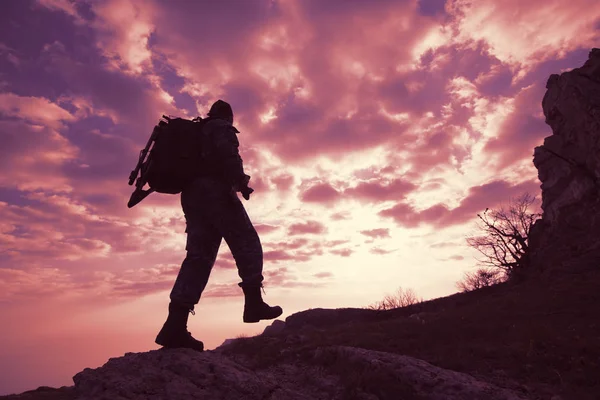 Bottom view silhouette of a male traveler with a backpack climbs up the mountains against a blue sky in white clouds. Concept of the unknown and lovers of mountain tourism
