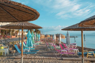Korfu Adası, Yunanistan 'daki inanılmaz körfez. Renkli şezlongları, yeşil dağlardaki ağaçları ve turistler için otelleri olan İyon deniz plajının güzel manzarası..