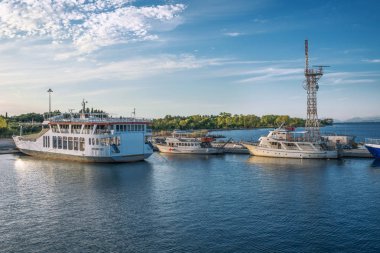 Kerkyra, Korfu Adası, Yunanistan - 4 Ekim 2019: İyon Denizi yakınlarındaki iki feribotun görüntüsü. Yeşil ağaçlı, güneşli, Korfu adasının güzel manzarası. Turistleri bekleyen tekneler.