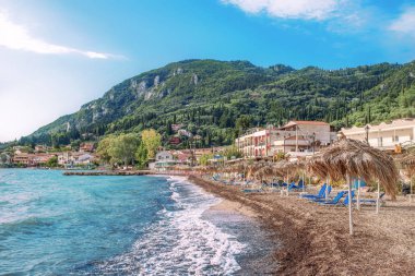 Korfu Adası, Yunanistan 'daki inanılmaz körfez. Renkli şezlongları, yeşil dağlardaki ağaçları ve turistler için otelleri olan İyon deniz plajının güzel manzarası..