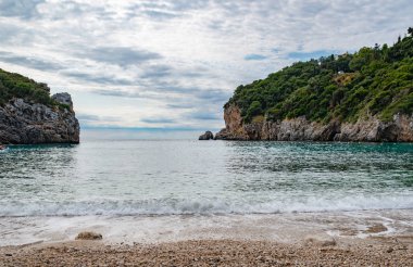 Korfu Adası, Yunanistan 'daki inanılmaz körfez. Renkli şezlongları, yeşil dağlardaki ağaçları ve turistler için otelleri olan İyon deniz plajının güzel manzarası..