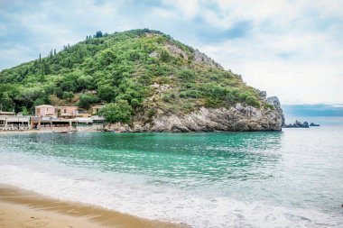 Korfu Adası, Yunanistan 'daki inanılmaz körfez. Renkli şezlongları, yeşil dağlardaki ağaçları ve turistler için otelleri olan İyon deniz plajının güzel manzarası..