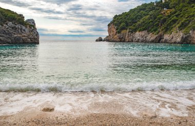 Korfu Adası, Yunanistan 'daki inanılmaz körfez. Renkli şezlongları, yeşil dağlardaki ağaçları ve turistler için otelleri olan İyon deniz plajının güzel manzarası..