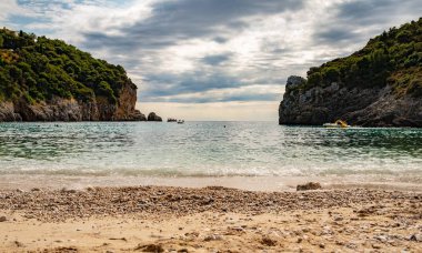 Yunanistan 'ın Corfu Adası' ndaki Paleokastritsa 'da kristal berrak suyla muhteşem körfez sahili. Ağaçlı iki kayanın güzel manzarası.
