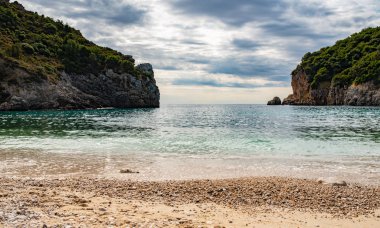 Korfu Adası, Yunanistan 'daki inanılmaz körfez. Renkli şezlongları, yeşil dağlardaki ağaçları ve turistler için otelleri olan İyon deniz plajının güzel manzarası..