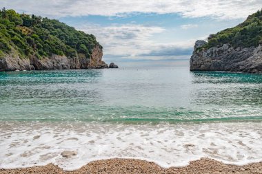 Yunanistan 'ın Corfu Adası' ndaki Paleokastritsa 'da kristal berrak suyla muhteşem körfez sahili. Ağaçlı iki kayanın güzel manzarası.