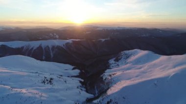 Akşam güneşiyle aydınlatılan Karlı Dağların Üzerinden Uçuş