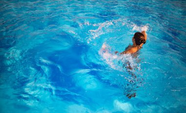 Kimliği belirlenemeyen güzel kız, parlak güneş ışığı altında havuzda mavi berrak suda mutlulukla sıçrıyor. Otelde ve denizde rahatlama kavramı. Reklam alanı