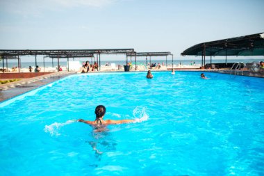 Kimliği belirlenemeyen güzel kız, parlak güneş ışığı altında havuzda mavi berrak suda mutlulukla sıçrıyor. Otelde ve denizde rahatlama kavramı. Reklam alanı