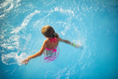 Parlak renkli mayo giyen mutlu küçük kız güneşli yaz günü güneşli bir havuzda yüzer. Aile tatili ve turizm konsepti. Reklam alanı