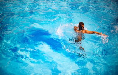 Kimliği belirlenemeyen güzel kız, parlak güneş ışığı altında havuzda mavi berrak suda mutlulukla sıçrıyor. Otelde ve denizde rahatlama kavramı. Reklam alanı