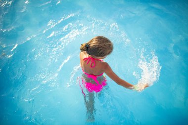 Parlak renkli mayo giyen mutlu küçük kız güneşli yaz günü güneşli bir havuzda yüzer. Aile tatili ve turizm konsepti. Reklam alanı