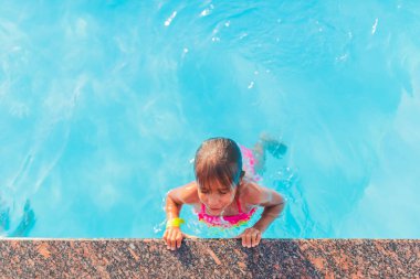 Yeşil mayo giymiş genç bir kız sıcak bir yaz gününde deniz kenarındaki otellerde tatil yaparken sıcak ve temiz su havuzundan çıkar. Sağlık ve aile tatillerinin iyileştirilmesi kavramı