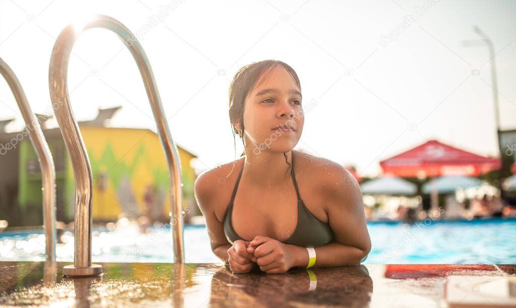 Happy pretty teenage girl emerged from the pool with clear blue water on a sunny warm summer day at the hotel during the holidays. Concept restoration of health and relaxation of children after school