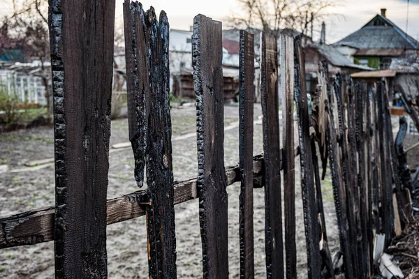Burnt fence boards after a fire in a private house. The consequences of not careful and thoughtless handling of fire.