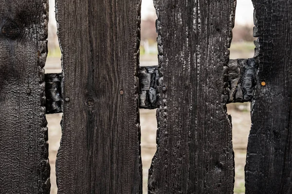 Burnt fence boards after a fire in a private house. The consequences of not careful and thoughtless handling of fire.
