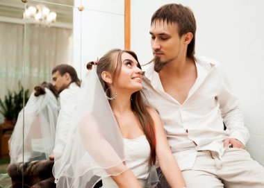 Nişanlısıyla koltukta oturan ve gülümseyen uzun saçlı mutlu genç bir kadının ön görüntüsü. Zarif beyaz kıyafetler giyen sevimli bir çift. Evlilik ve ilişkiler kavramı.