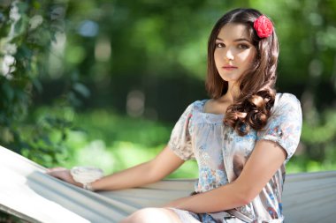 Ağaç hamak yatağında dinlenen, saçları çiçekli çekici bir kadın. Zarif elbiseli hoş bir kız bahar bahçesinde dışarıda vakit geçiriyor. Güzellik, zarafet ve doğa kavramı.