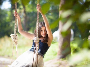 Sallanan salıncakta sallanan zarif bir bayanın ön görüntüsü. Şık elbiseli, elinde iplerle sevimli bir gülümsemeyle kameraya bakan hoş bir kız. Güzellik, neşe ve rahatlık kavramı.