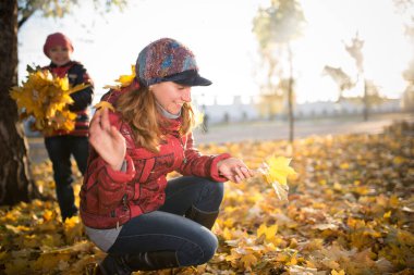 Sevimli anne ve neşeli kız güneşli bir günde yürüyüş sırasında sarı akçaağaç yapraklarıyla parkta oynuyorlar. Aile zamanı kavramları ve eğlence gelenekleri