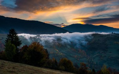Tepe kenarındaki çayır üzerinde güzel bulutlu gökyüzü manzarası. Duman ve arka planda çarpıcı parlak gökyüzü olan görkemli dağ manzarası. Doğa ve şafak kavramı.