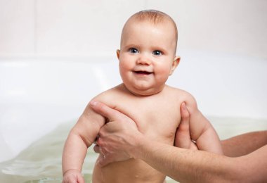 Dikkatli, bilinmeyen bir annenin elleri küçük, komik, büyük gözlü bir bebeği tutuyor. Çocuklar üzerinde bakım ve hijyen kavramı.