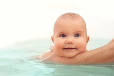 Dikkatli, bilinmeyen bir annenin elleri küçük, komik, büyük gözlü bir bebeği tutuyor. Çocuklar üzerinde bakım ve hijyen kavramı.