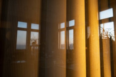 Günbatımının ışığında pencerenin dışındaki dikey geniş perdeler ofis pencerelerinin yansımasıdır..