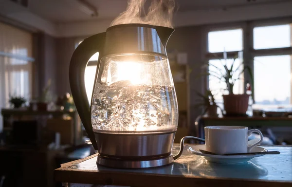 窓から差し込む夕日を背景に 透明感のある湯釜が沸いてくる コーヒー休憩と作業日の終わりの概念 — ストック写真