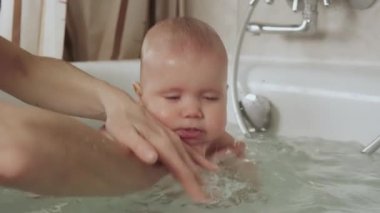 Dikkatli, bilinmeyen bir annenin elleri küçük, komik, büyük gözlü bir bebeği tutuyor. Çocuklar üzerinde bakım ve hijyen kavramı. 4K UHD hala video kamera, 2x yavaş çekim.