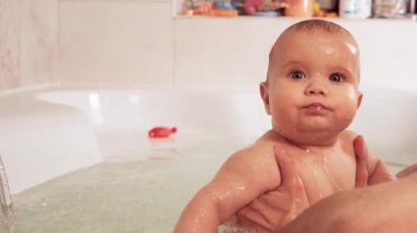 Dikkatli, bilinmeyen bir annenin elleri küçük, komik, büyük gözlü bir bebeği tutuyor. Çocuklar üzerinde bakım ve hijyen kavramı. 4K UHD hala video kamera, 2x yavaş çekim.