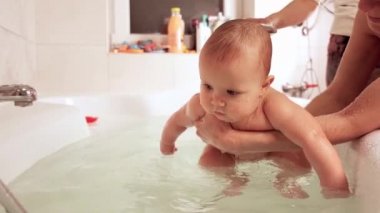 Dikkatli, bilinmeyen bir annenin elleri küçük, komik, büyük gözlü bir bebeği tutuyor. Çocuklar üzerinde bakım ve hijyen kavramı. 4K UHD hala video kamera, 2x yavaş çekim.